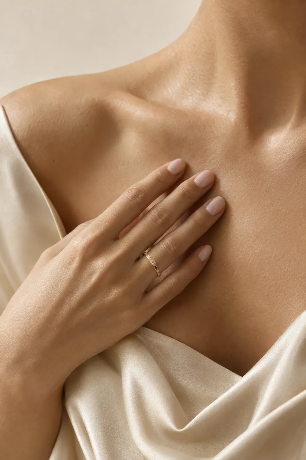 Detail of a hand with a gold ring on the collarbone and ivory silk fabric